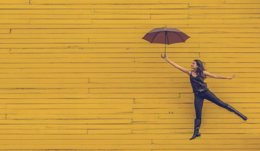woman against yellow background carried away by umbrella
