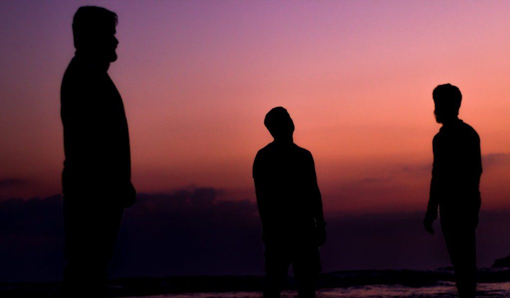 three people standing in shadow with sunset behind