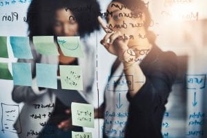 two woman discussing at white board