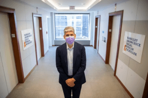 A man with a mask stands in an office hallway