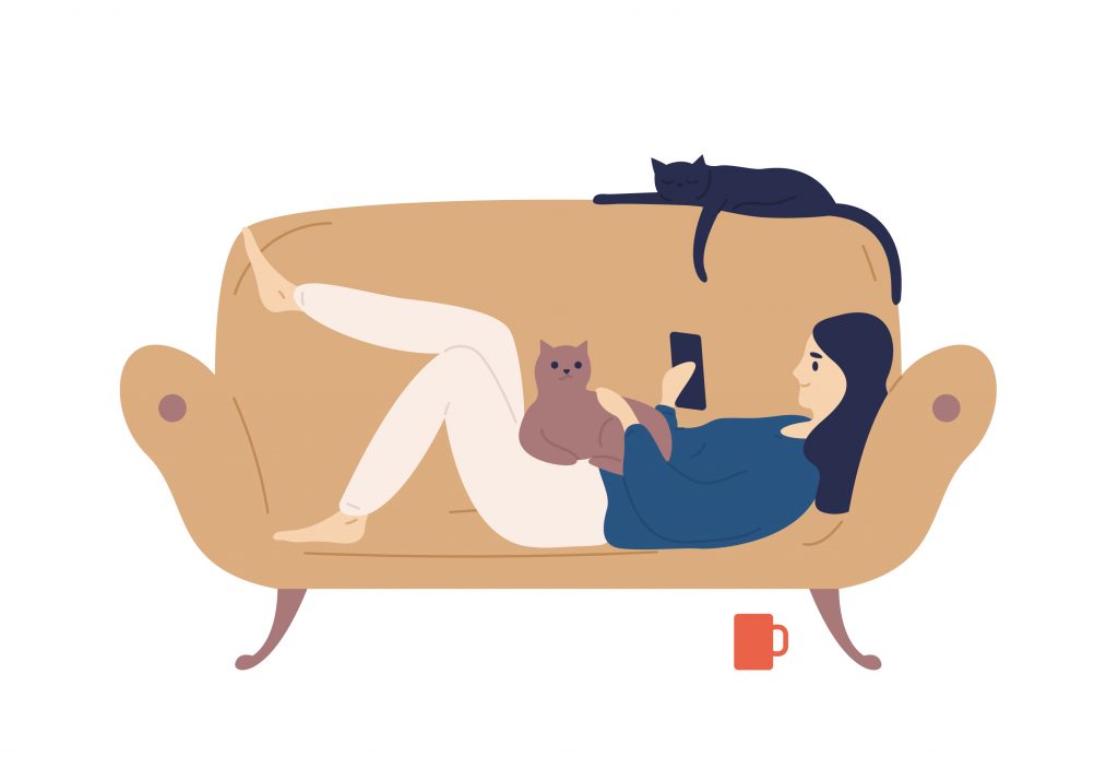 Image of a feminine person lounging on a couch, using a mobile device while cats rest beside her.