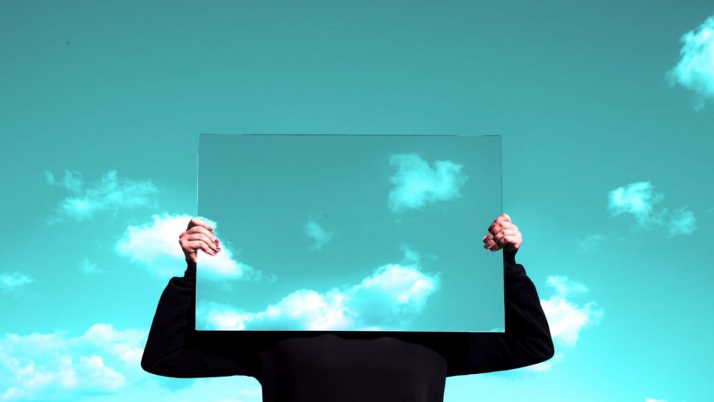 A figure holds up a mirror in an image advertising fast company's article on changing perceptions, including Dr. Michaela Simpson of the NeuroLeadership Institute.