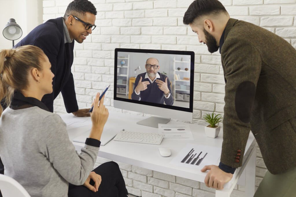 Three people gather around a desk where they talk to another man on a video chat