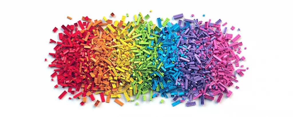 A pile of legos on a white backdrop are sorted in the colors of a rainbow