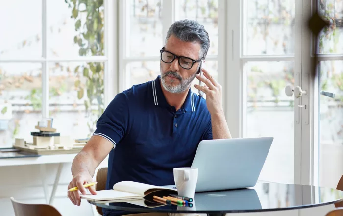 A man works from home with his laptop, headset, and notebook