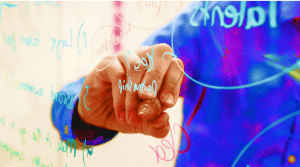 A man writes on a translucent white board