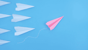 A pink paper airplane takes the lead over white ones