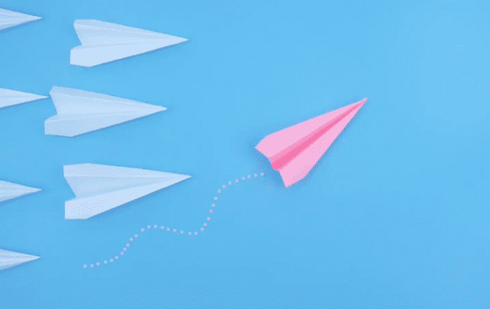 A pink paper airplane takes the lead over white ones
